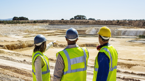 Architects and construction worker examining quarry against clear sky