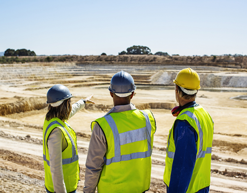 Architects and construction worker examining quarry against clear sky
