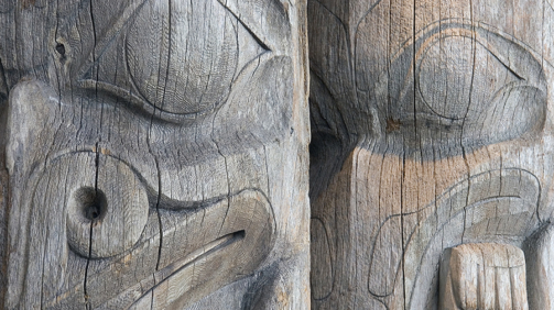 Detail of two faces on a pair of old, worn, unpainted, wooden West Coast Indian totem poles in a Vancouver, British Columbia park.