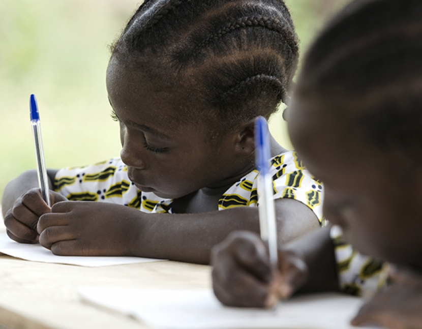 Gorgeous black African ethnicity students writing their essay in an African school in Bamako, Mali. They're holding blue pens to write down their homework whilst sitting in their desk.