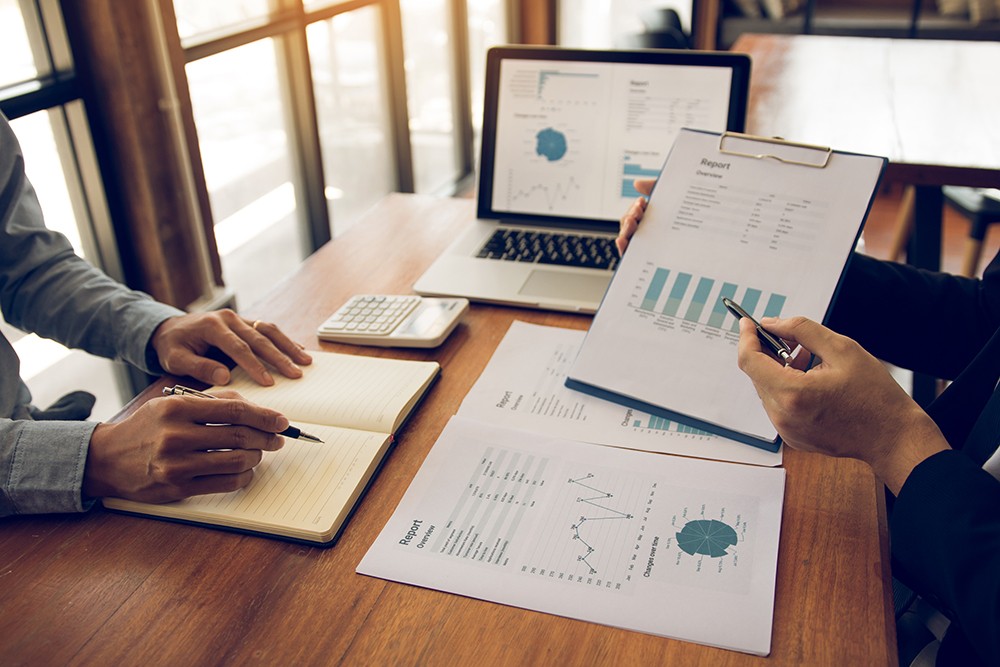 Two business partnership coworkers analysis strategy with discussing a financial planning graph and company budget during a budget meeting in office room. | TeamsynerG Global Consulting