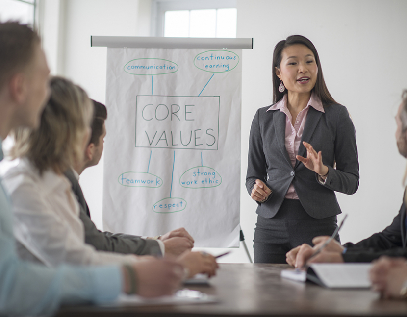 A multi-ethnic group of business professionals are gathered in the conference room for a meeting. The new inters and trainees are learning the core values of the company.