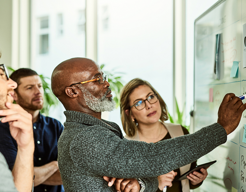 Cropped shot of a diverse group of businesspeople standing and using a white board to strategise in the office