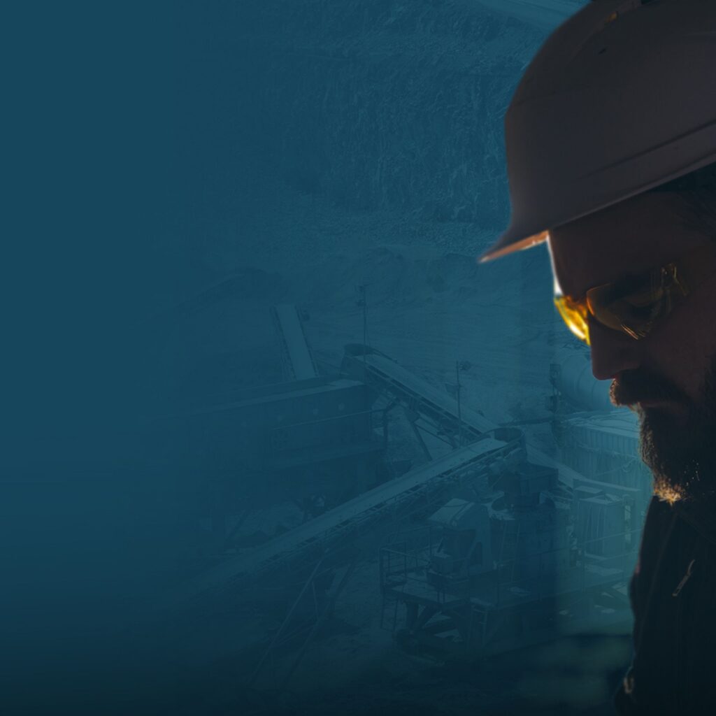 Profile view of a worker wearing a hard hat and safety glasses at an industrial site.