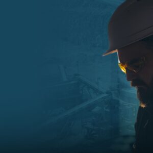 National-Day-of-Mourning-and-World-Day-for-Safety-and-Health-at-Work-1920x1080 | TeamsynerG Global Consulting Profile view of a worker wearing a hard hat and safety glasses at an industrial site.