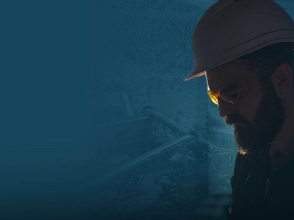 Profile view of a worker wearing a hard hat and safety glasses at an industrial site.