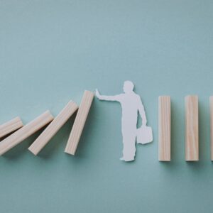 White paper silhouette of a person pushing a domino to stop a falling chain of wooden blocks on a blue background.