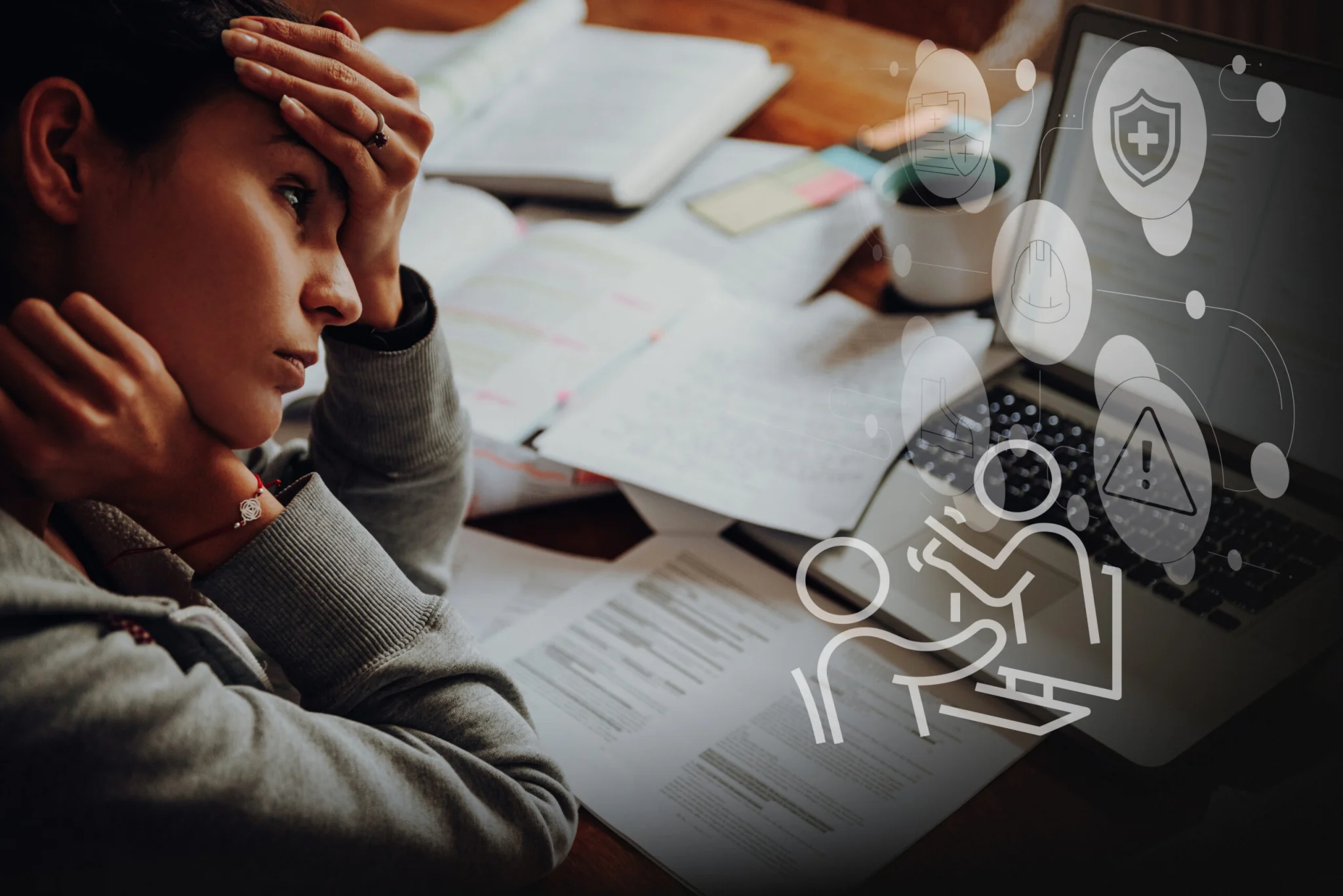 Person sits at a desk with open papers, holding their head in distress while studying. A laptop and notes are on the desk with faint digital icons overlaid on the screen.